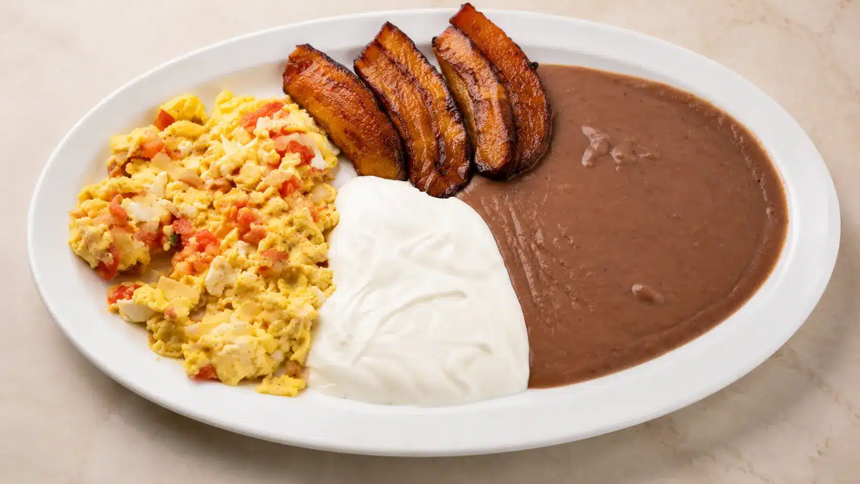 Scrambled eggs, fried plantains, refried beans, and sour cream plate.