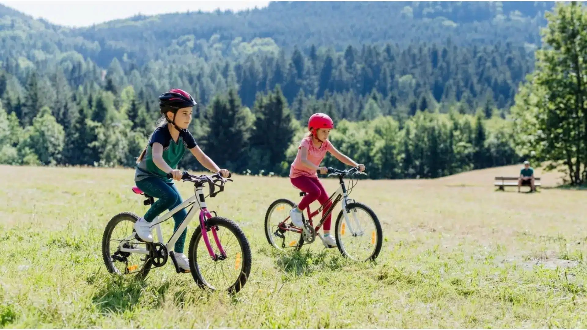 Children riding bicycles with helmets on a grassy field while an adult supervises nearby.