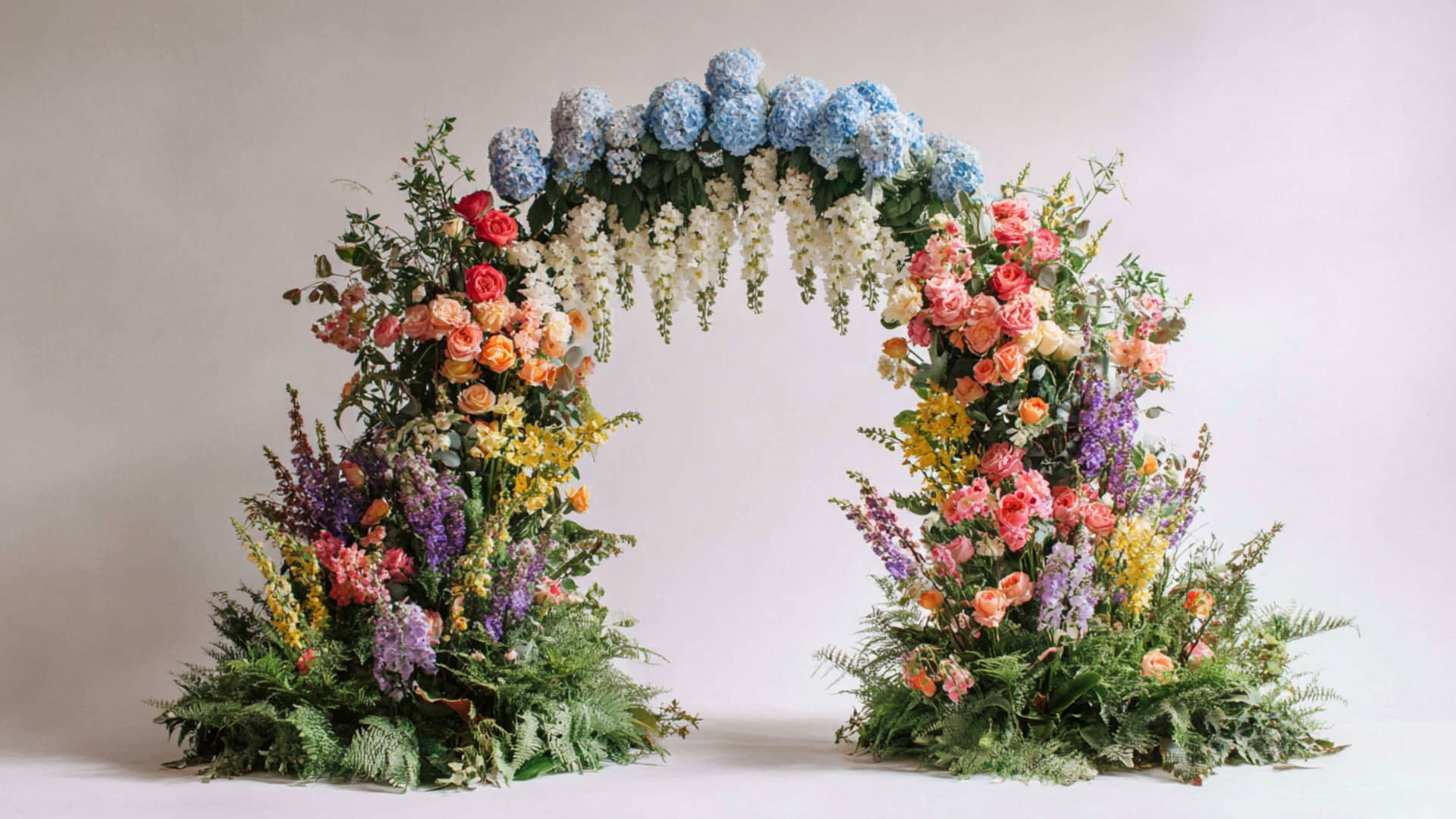 Colorful garden wedding arch with blue hydrangeas and mixed blooms on white set.