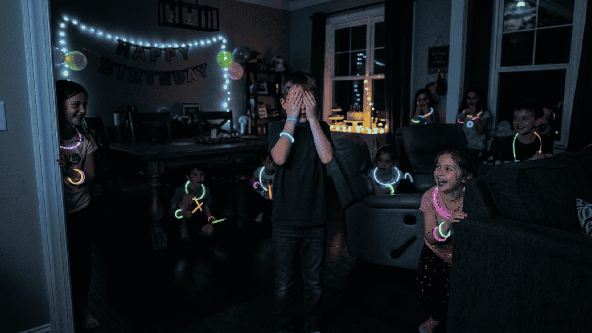 Dimly lit room with kids in neon glow necklaces playing hide and seek; seeker counts in the center.