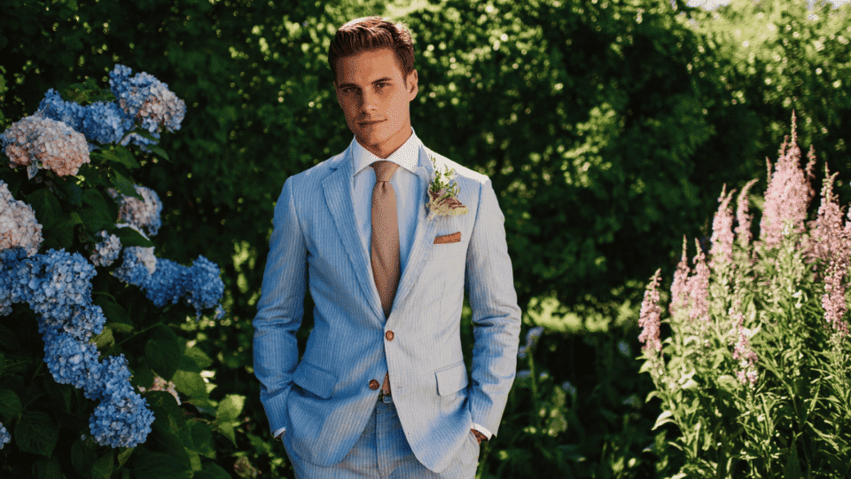 Groom in a soft-toned pastel suit with a white shirt, standing out in a summer wedding setting.
