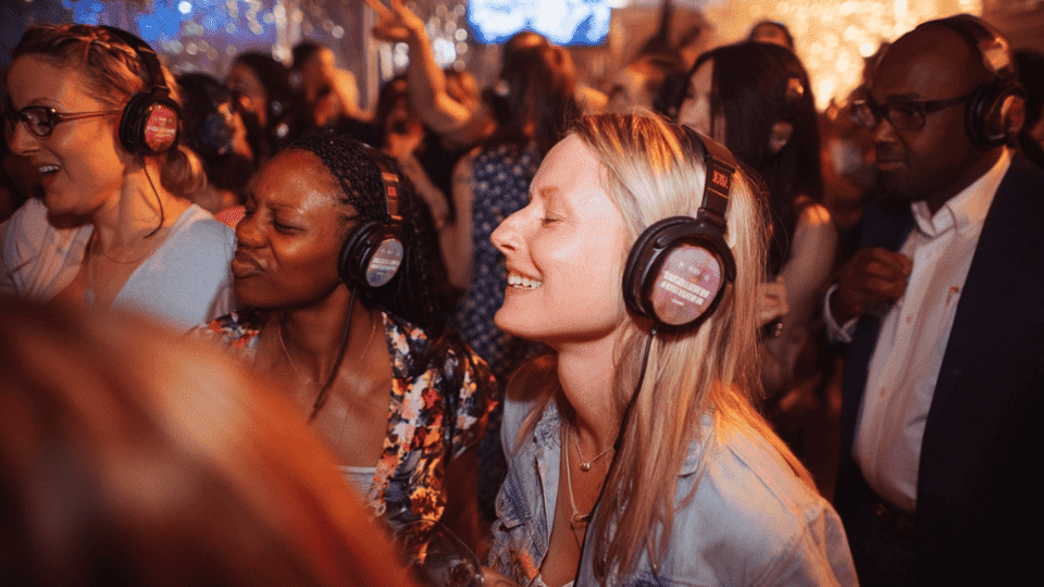 Guests at a silent disco wearing wireless headphones, dancing in a wedding reception with festive decor