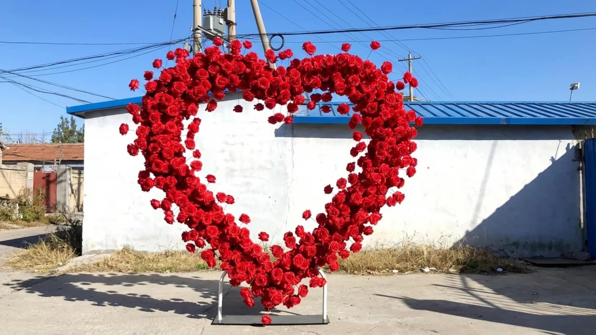 Heart-shaped red rose wedding arch display set outdoors against a simple wall