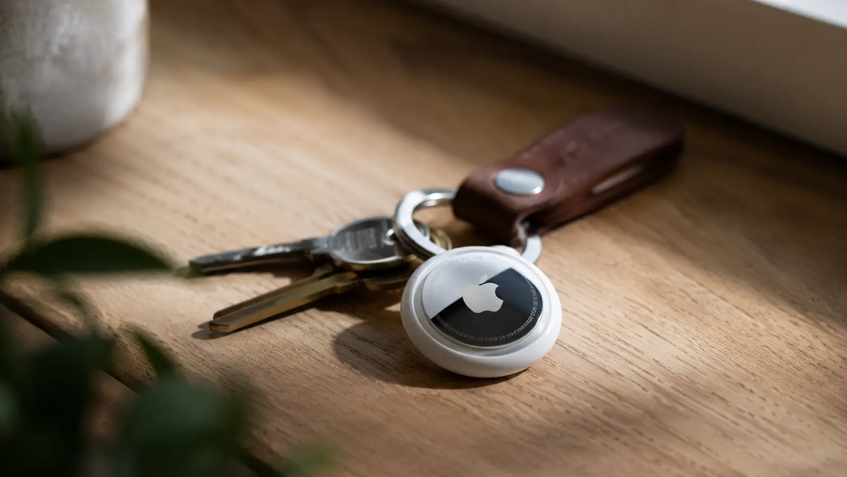 Keys on a wooden surface with an Apple AirTag attached to a leather keychain.