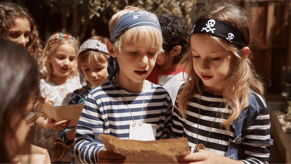 Kids on a treasure hunt searching for clues and finding a hidden treasure box at a birthday party