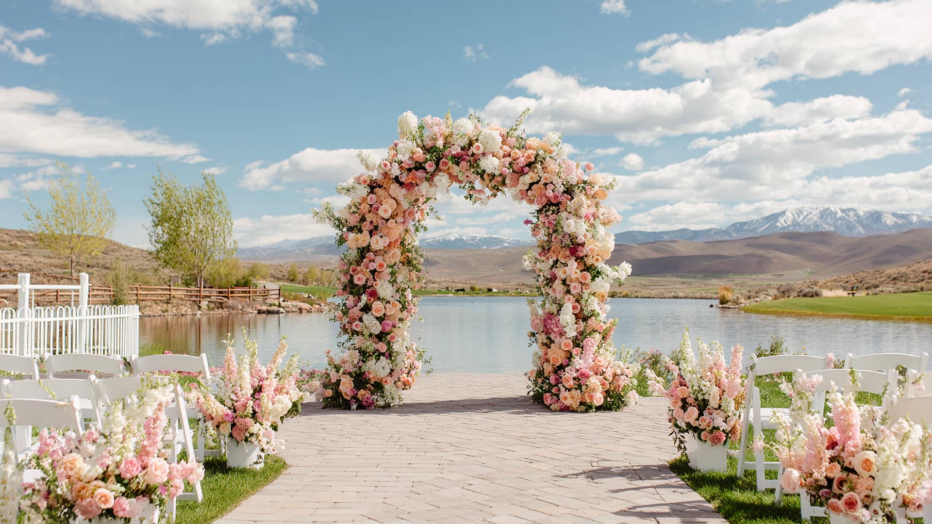 Pastel floral wedding arch by a lake with mountain views and aisle flowers ready.
