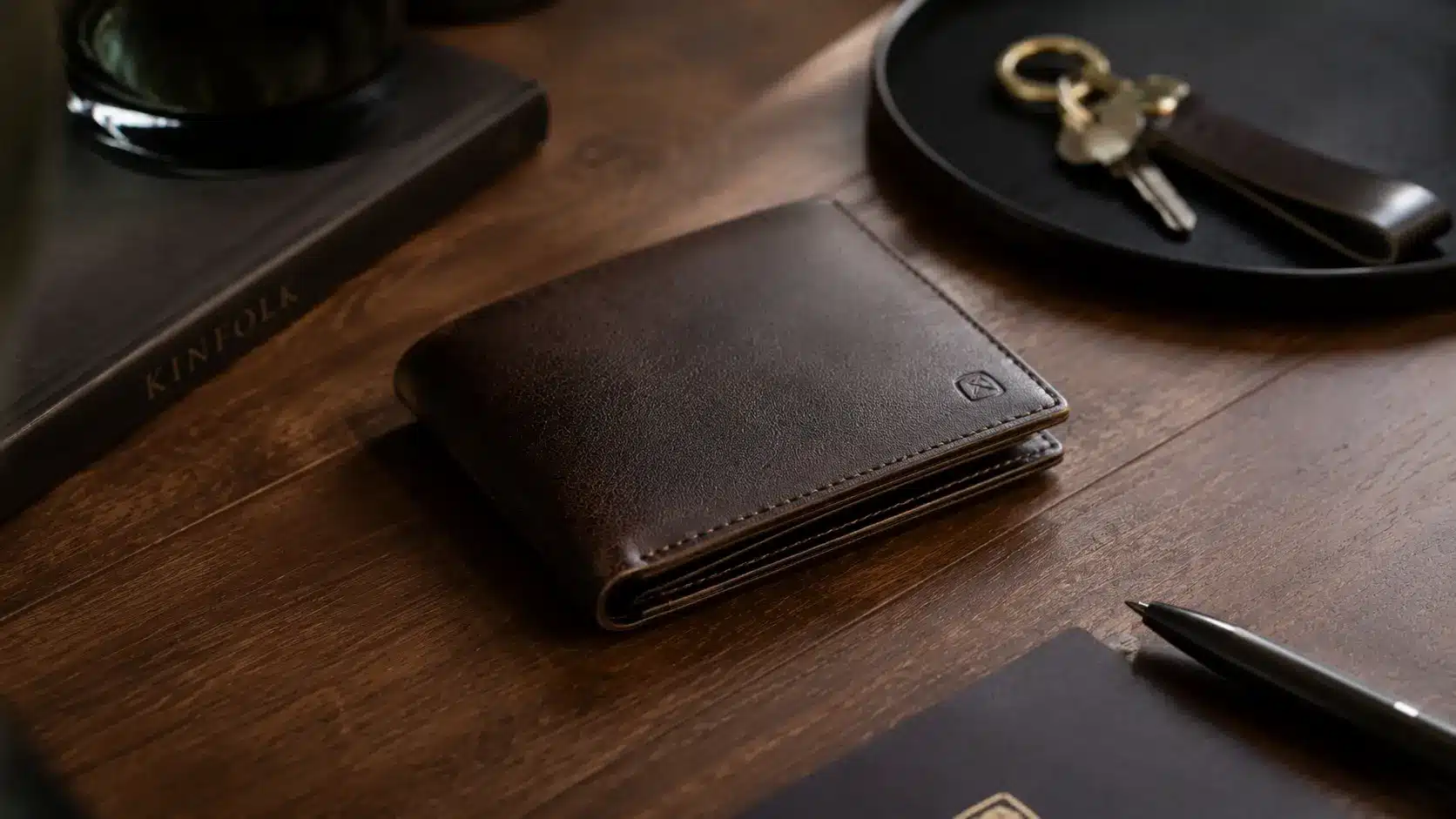Premium leather wallet on a wooden surface next to a key tray, notebook, and pen.