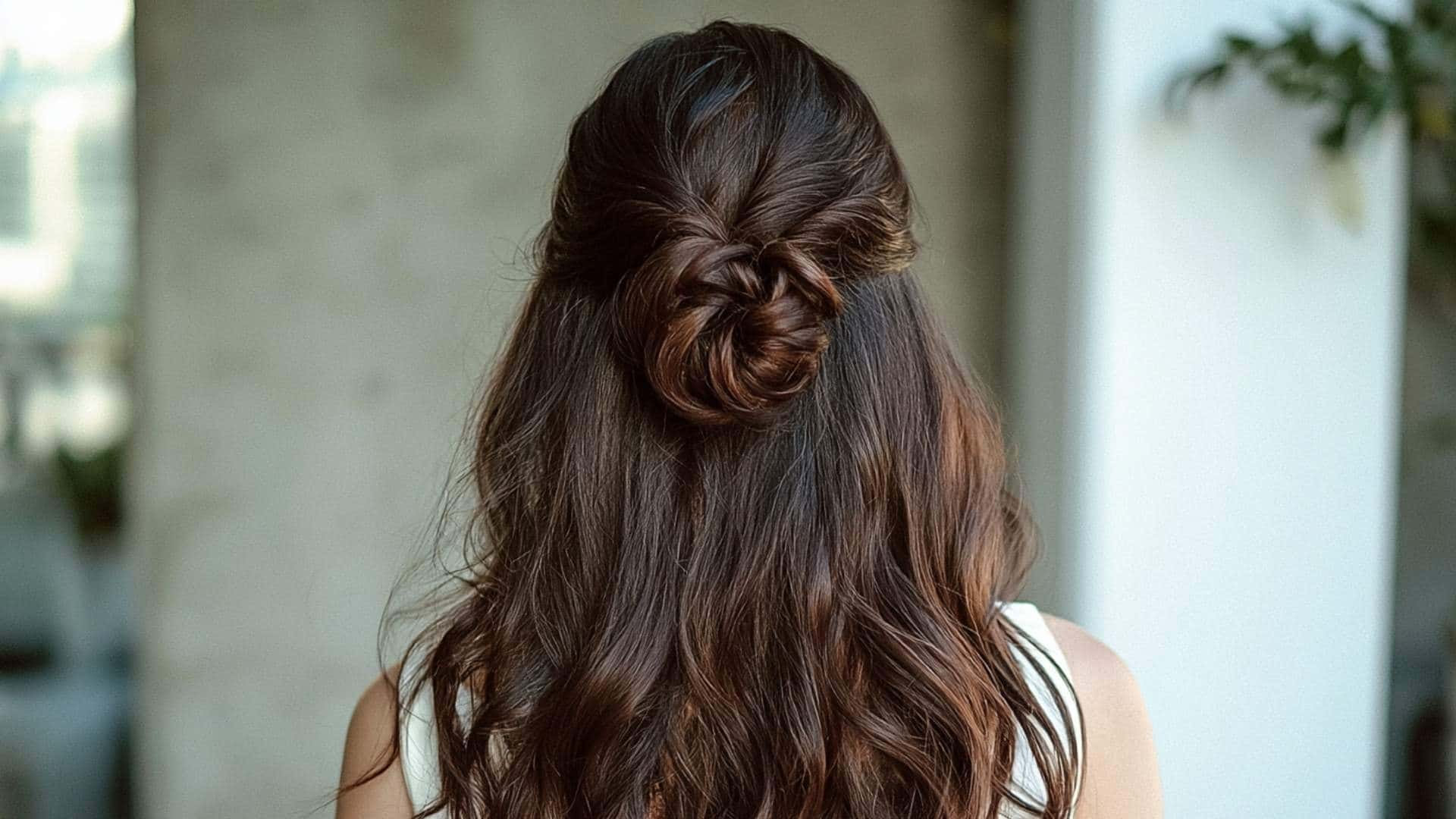 Back view of a bride with a small half up top knot above long softly waved hair with individual strands visible