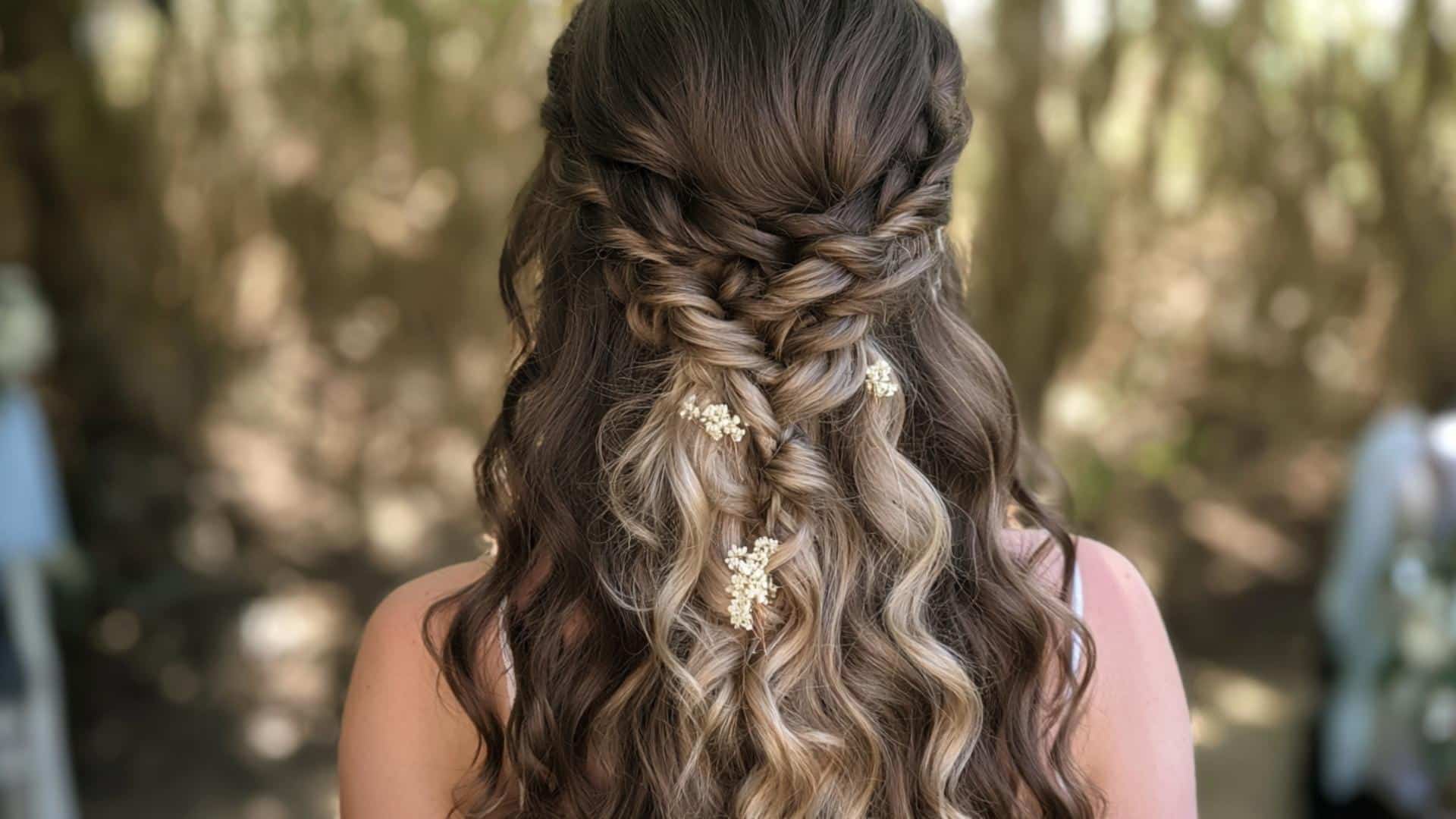 Back view of a bride with several small crown plaits woven into long half up curled hair with natural flyaways