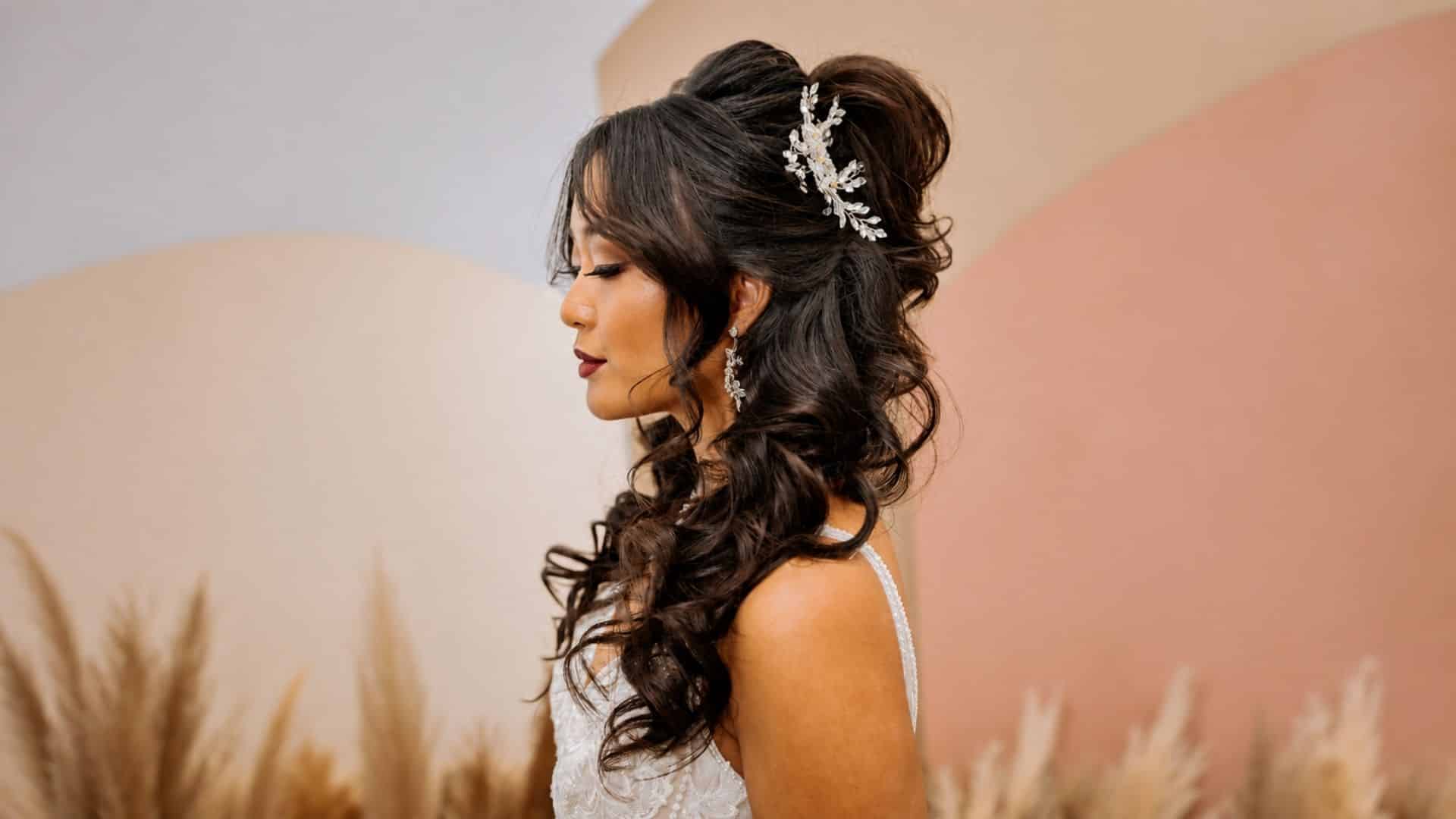 Bride in profile wearing a twisted half up half down hairstyle with cascading curls and a delicate crystal hairpiece