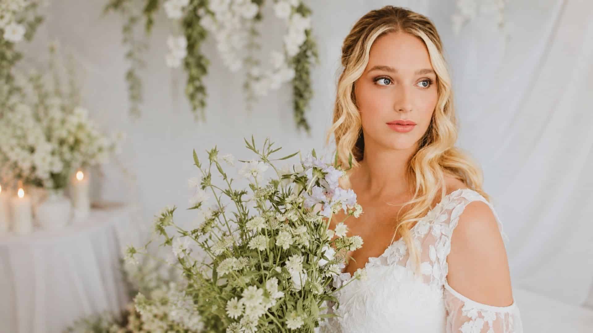 Bride with money piece highlights and a half up half down hairstyle, soft blonde waves, lace gown, and wildflower bouquet
