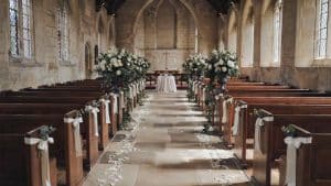 Church aisle with ribbon pew bows and altar flanked by white floral urns