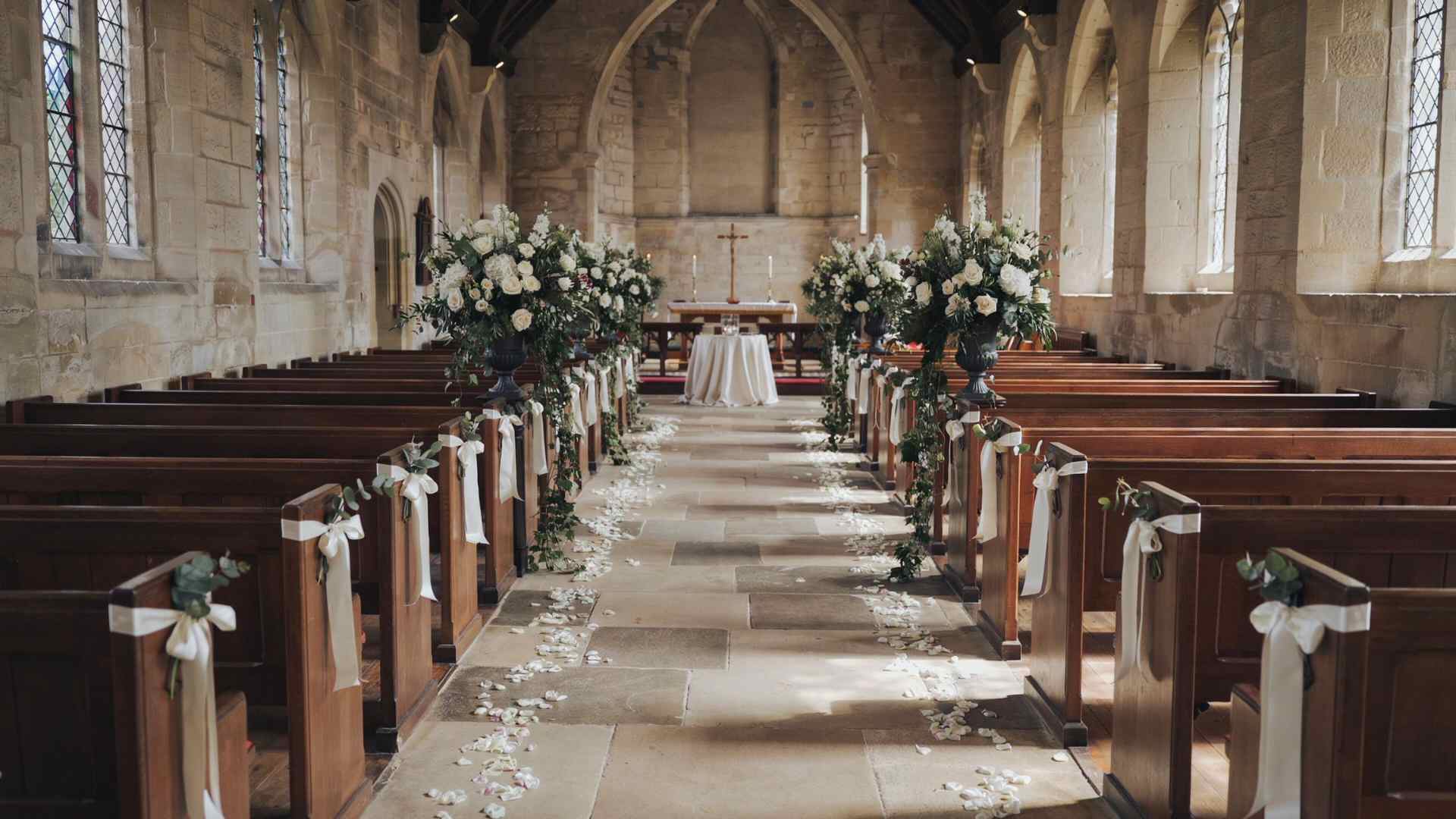 Church aisle with ribbon pew bows and altar flanked by white floral urns