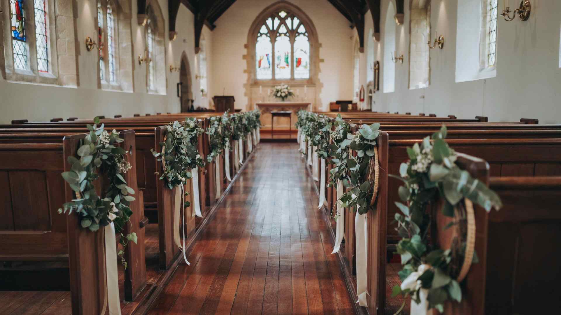Faux greenery hoops with ribbon hanging from church pews