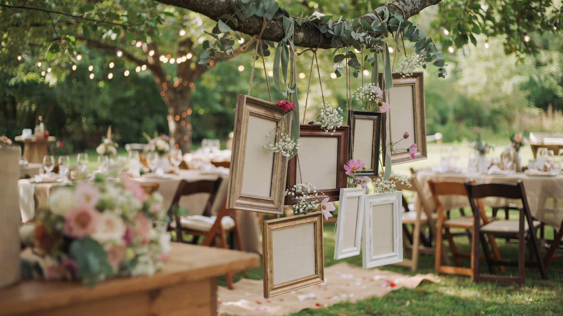 Hanging vintage frames decorated with eucalyptus and small flowers create a charming outdoor wedding photo display