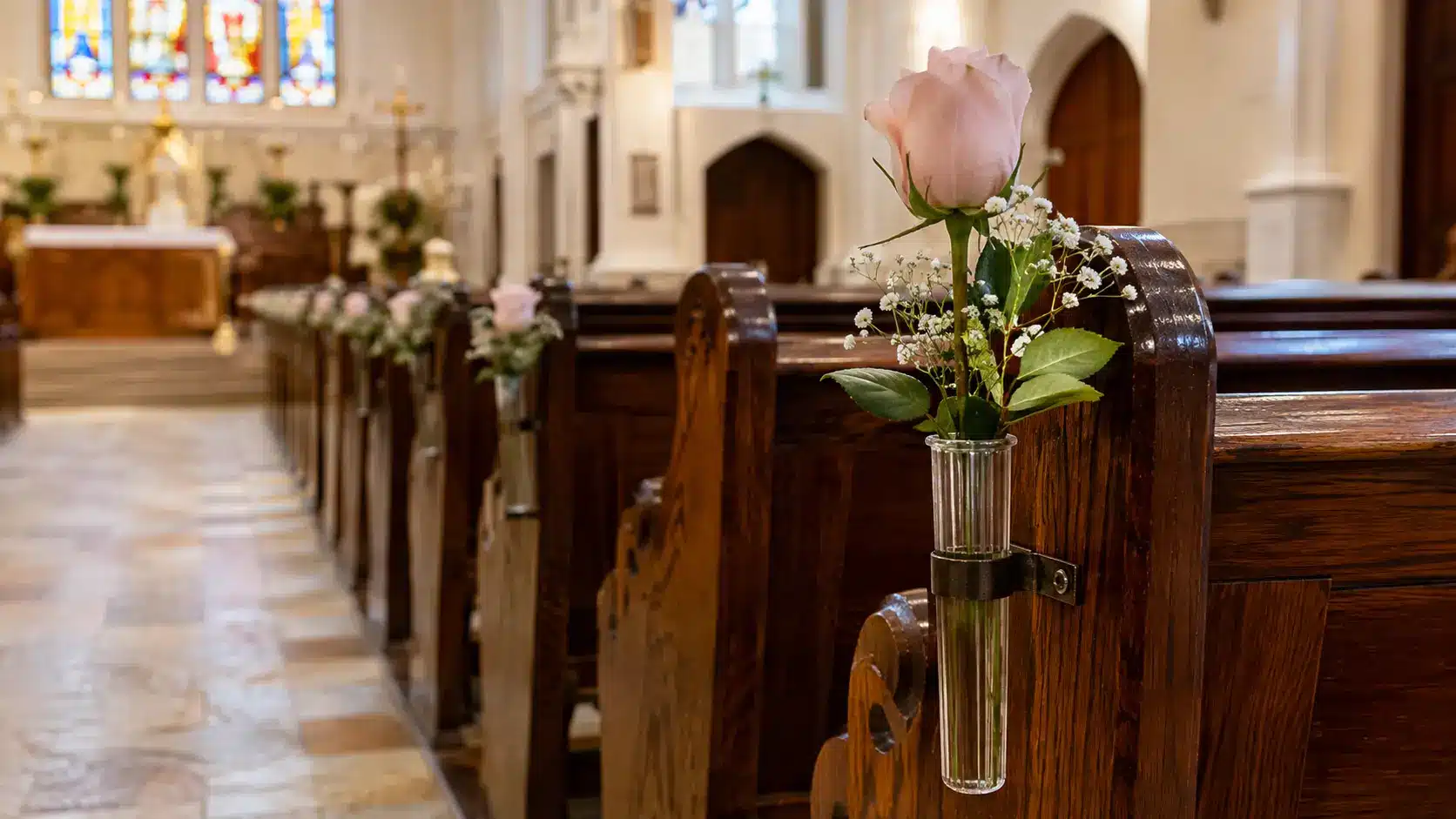 Single flower stems in small vases attached to church pews