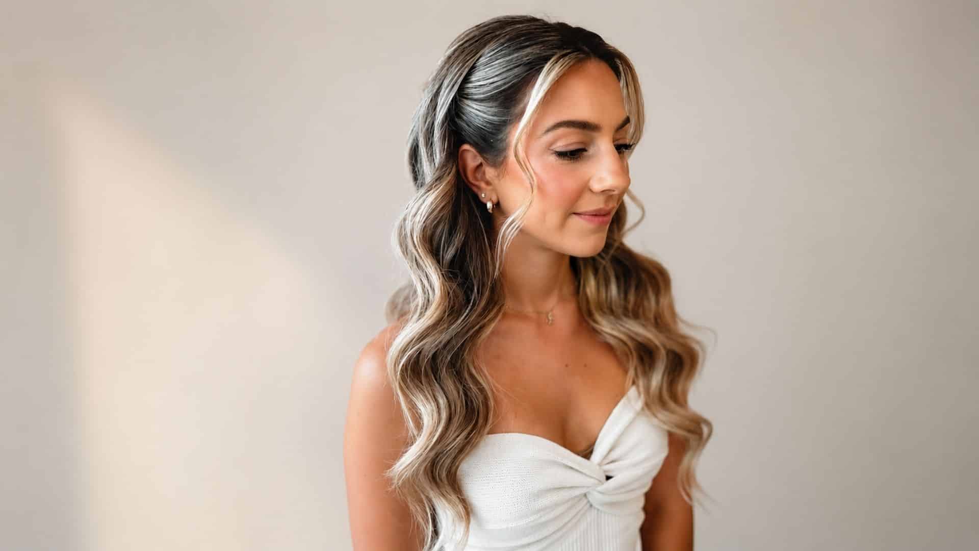 Soft romantic bridal curls with highlighted waves, pinned back sections, and loose strands framing the face on a backdrop
