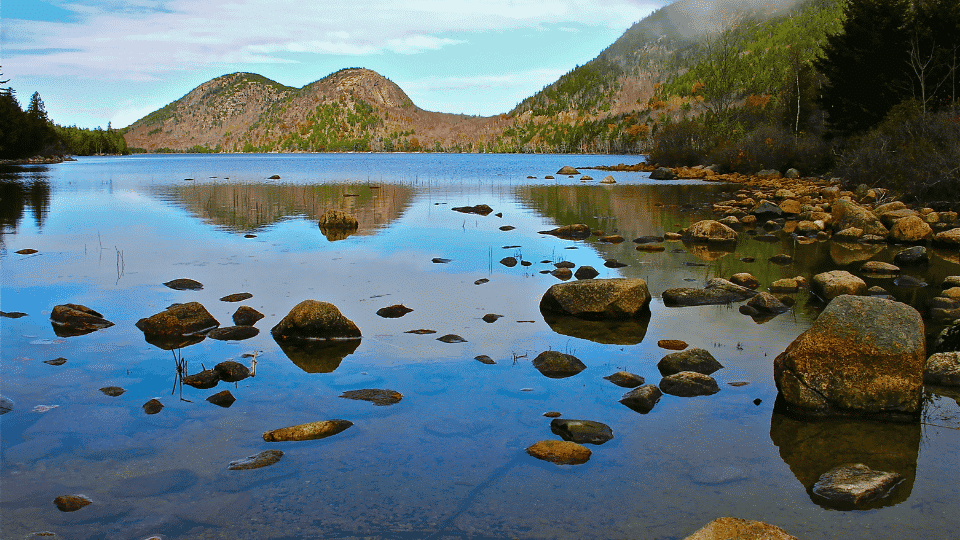 Rugged coastal rocks, blue ocean water, and forested hills in Acadia National Park, Maine.