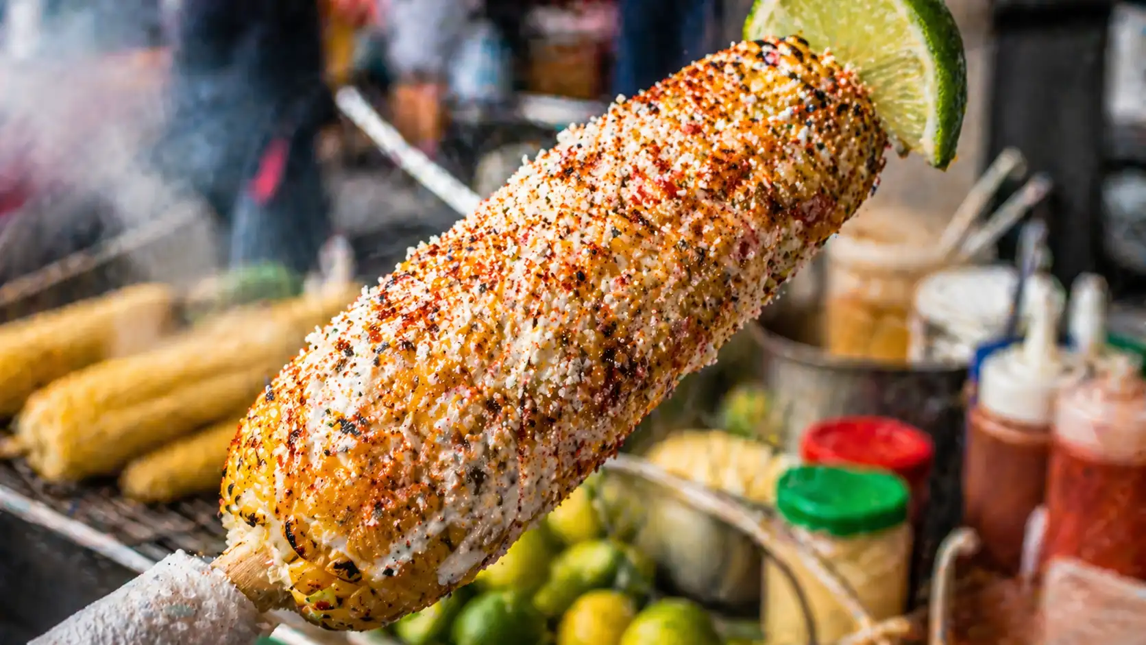 Grilled Mexican elote coated with creamy sauce, crumbled cheese, chili powder, and served with a lime wedge.