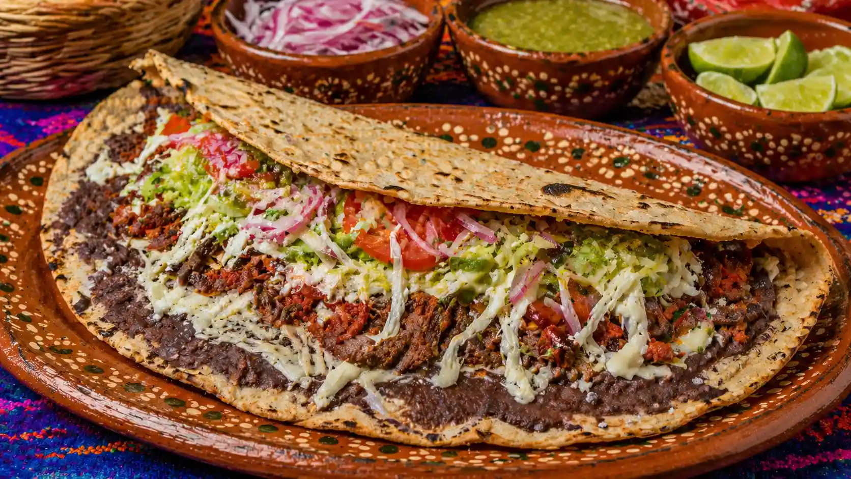 Large folded tlayuda topped with black beans, chorizo, shredded beef, melted cheese, lettuce, tomato, and salsa.