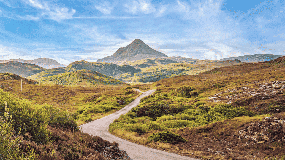 Winding North Coast 500 road surrounded by rugged mountains and dramatic Scottish coastal scenery.
