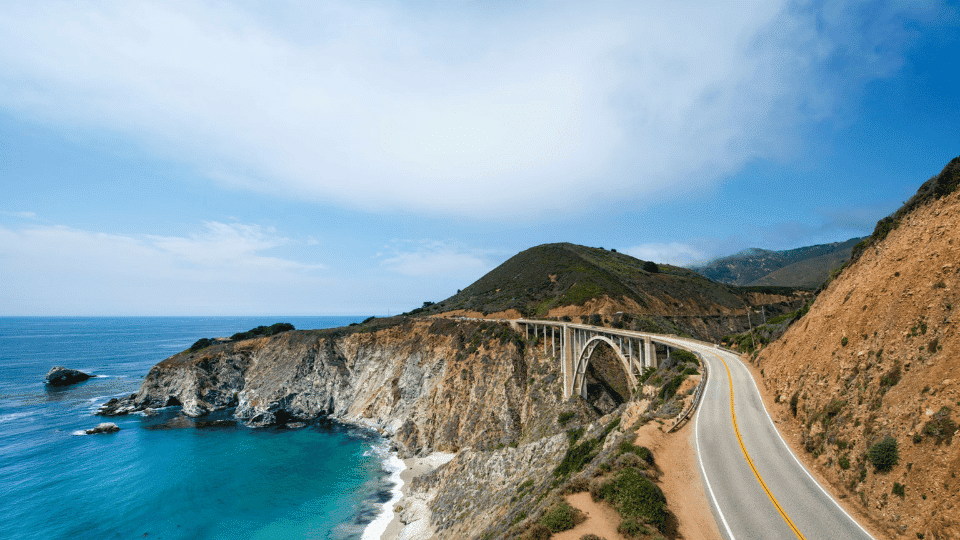Scenic Pacific Coast Highway winding beside rugged cliffs and blue ocean along California's coastline.