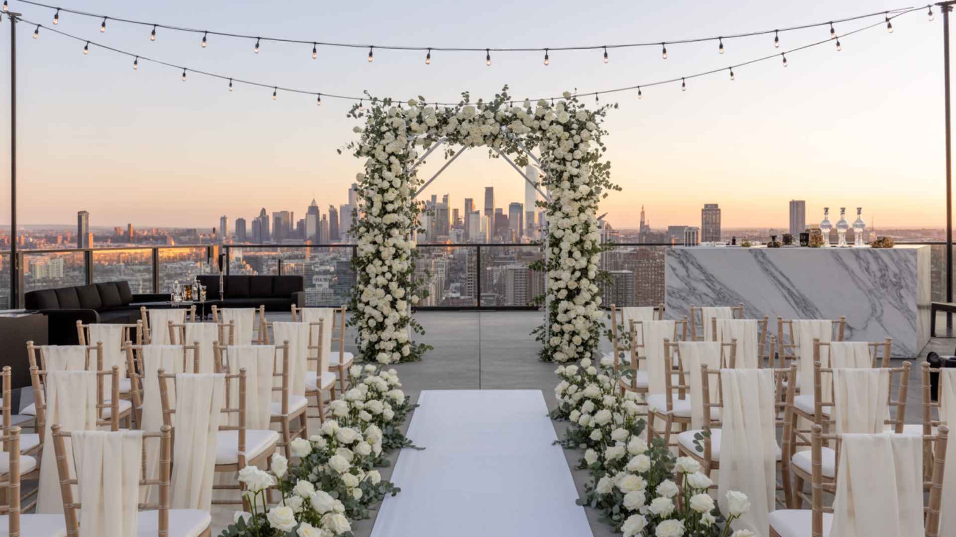 Rooftop wedding with city skyline, string lights, low lounge furniture, sunset.