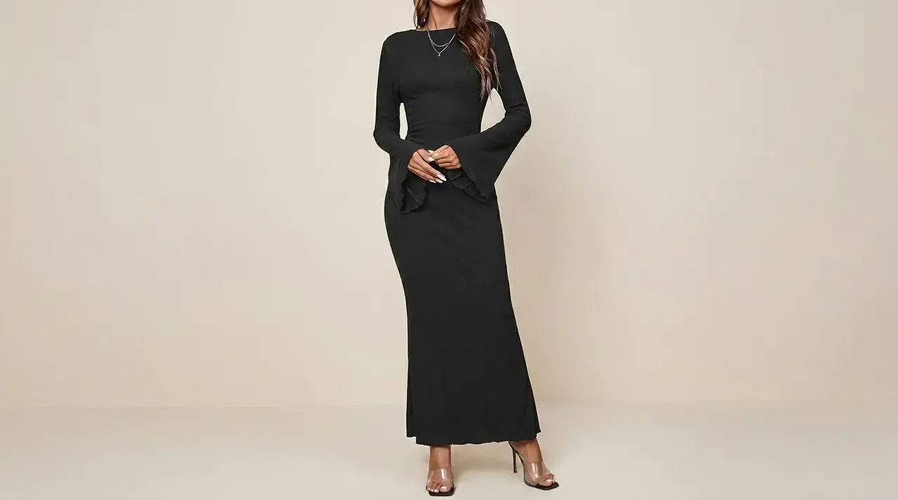 Woman wearing a long black bodycon dress with flared sleeves and open-toe heels against a beige backdrop.